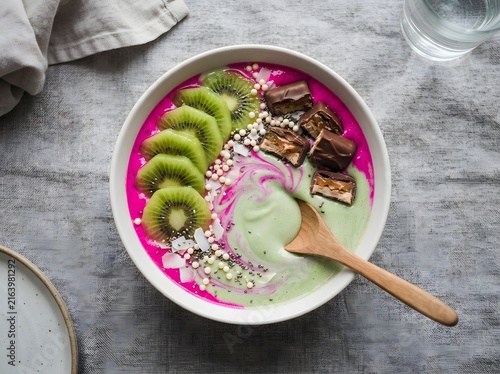 Pink and green smoothie bowl topped with sliced kiwi fruit and chocolate pieces