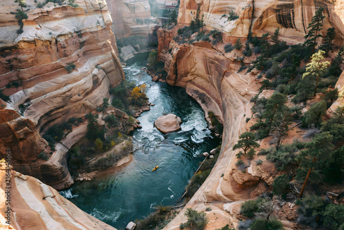 Aerial view of a winding river flowing through a deep canyon with towering orange sandstone rock walls and lush green pine trees along banks