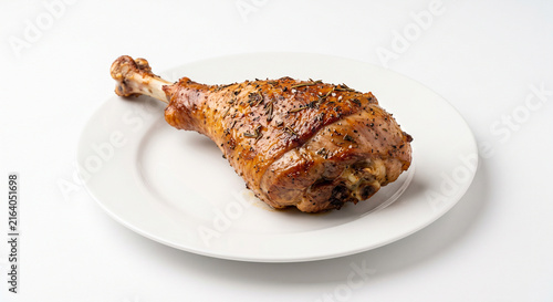 Delicious roasted turkey leg or chicken drumstick seasoned with herbs and spices on a white plate isolated on a white background with copy space