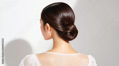 Woman with shiny brown hair in neat bun hairstyle wearing sheer white top