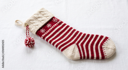 Knitted red and white striped Christmas stocking with a cabled cuff and pompom detail on a white background with copy space