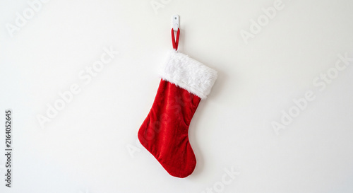 Red velvet Christmas stocking with white faux fur cuff hanging on a white wall with a hook vertical copy space