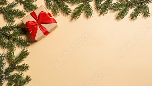 Festive Christmas Gift Box with Red Ribbon and Fir Branches on Beige Background with Copy Space
