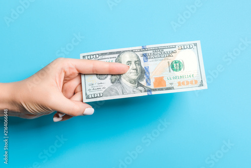 Female hand giving a bundle of dollar bills on blue background. Power and wealth concept