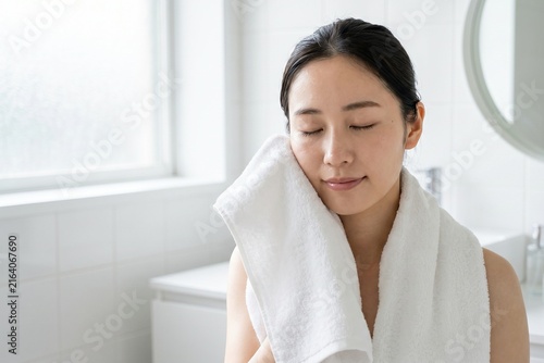 明るい洗面所で顔を拭く若い女性（ライフスタイル・健康・お風呂上がり・コピースペース）