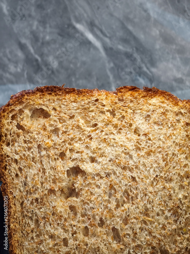 Toasted Whole Wheat Crust Close-Up. Artisanal roasted grain bread showing dense crumb texture and crisp dark brown crust on slate gray background.