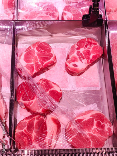 Display of fresh raw pork slices showing marbling. Premium-quality, fresh raw meat slices with beautiful marbling, wrapped in protective plastic and displayed in a supermarket refrigerated showcase.