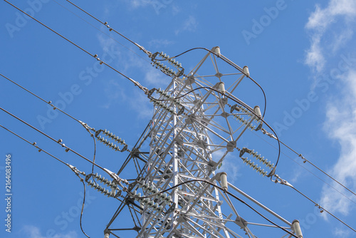 Low-angle view of a high-voltage lattice transmission tower with jumper loops bridging dead-end lines and disc insulators against a blue sky.