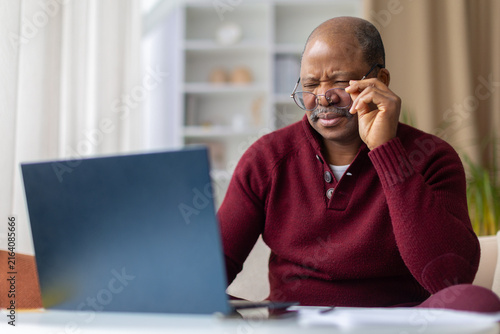 Fotografie Mature black man straining eyes while adjusting glasses at laptop, wearing maroo