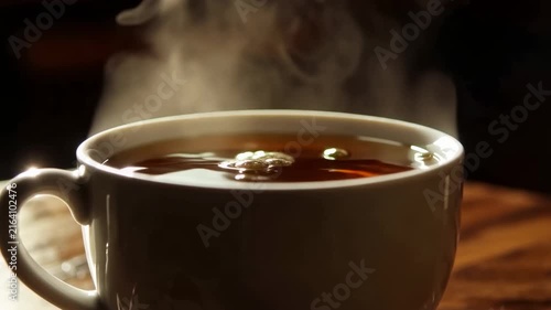 Hot coffee being poured into a white ceramic cup on a wooden table, steam rising from the freshly brewed beverage in a cozy indoor setting