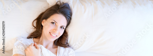 Fotografie Panoramic crop of a smiling young caucasian woman awake in a bright hotel bedroom with copy space, suited to travel and resort promotion