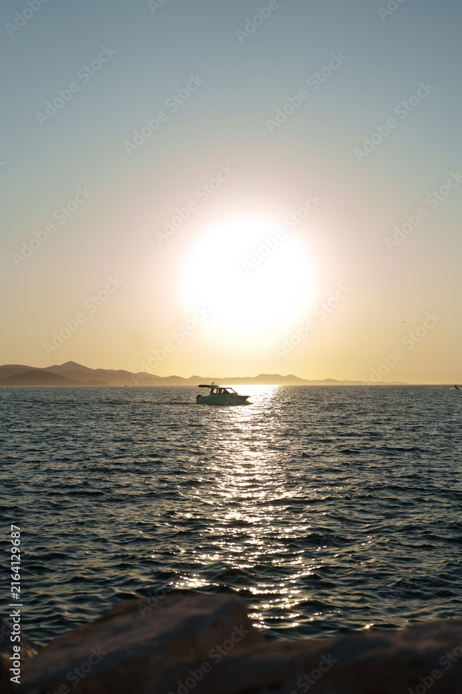 Obraz premium Beautiful golden sunset over a calm lake with a boat on the water, creating a peaceful natural landscape in Croatia.