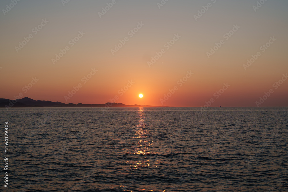 Fototapeta premium Beautiful golden sunset over a calm lake with a boat on the water, creating a peaceful natural landscape in Croatia.