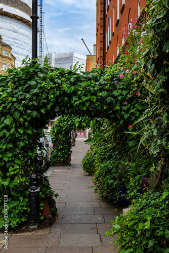 Canvas Print London - 07 22 2022: Kemble Street walkway with ivy‑covered arches and flowering