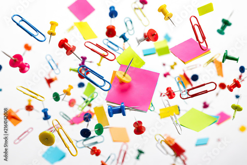 A vibrant collection of colorful paper clips and sticky notes floats in mid-air against a stark white background.