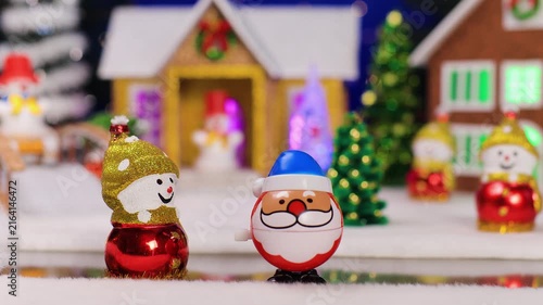 A quirky Santa Claus jumps up to a snowman against a blurred background of a small town