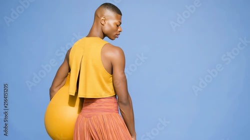 Fashion portrait of a male model holding a large yellow sphere against a solid blue studio backdrop for editorial background and banner design
