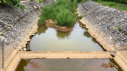 Canvas Print An artificial drainage channel with stagnant water, reinforced concrete slopes, and dense grassy vegetation