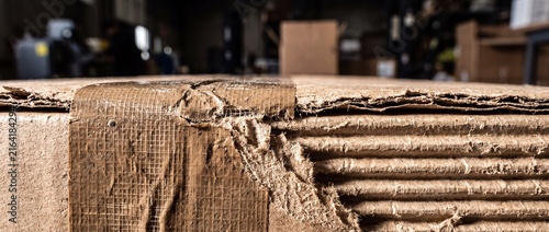 Close up of torn brown packaging tape on corrugated cardboard box displaying frayed paper fibers and layered structural composition