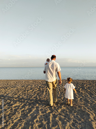 Father walking with son in his arms and daughter by the lake shore