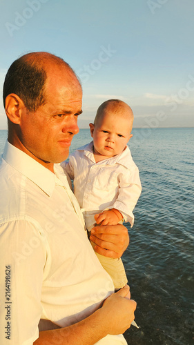 Father holding young son in his arms by a lake at sunset close-up
