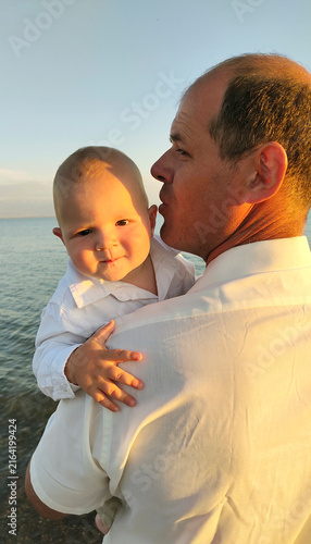 Father holding young son in his arms by a lake at sunset close-up