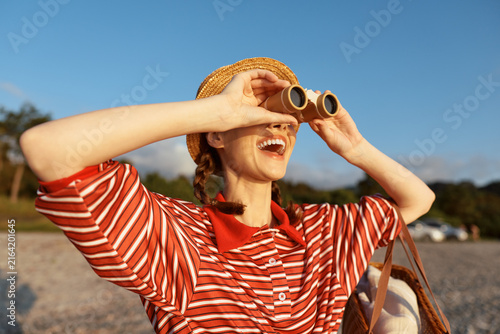 Bild auf Leinwand Happy woman looking through binoculars at the sunny beach