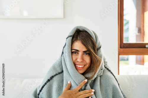 A white woman wrapped in a blanket smiles warmly indoors