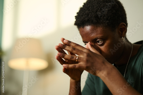 Canvas Print Young African American woman looking down with worried expression, holding hands near face