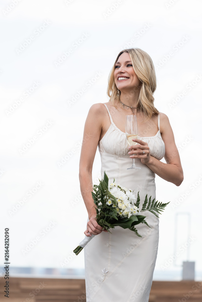 Fototapeta premium Young bride on her wedding day joyfully holds a bouquet while enjoying the view