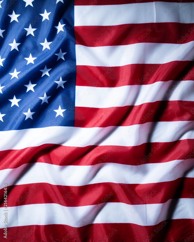 Fototapeta premium Close up of a draped American flag with stars and stripes, strong fabric folds and dramatic light creating a classic patriotic background.