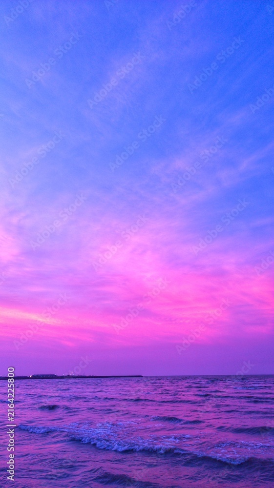 Fototapeta premium Vibrant purple and pink sunset over a calm ocean horizon, creating a dreamy seascape background with dramatic clouds and colorful twilight reflections.