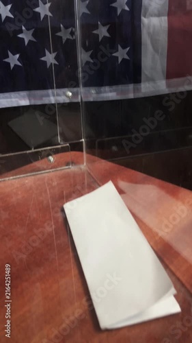 POV of voter inserting ballot sheet into slot of transparent box at US polling place
