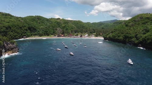 Drone view flying over a beautiful bay with traditional boats and a white sand beach in bali