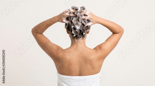 Young woman washing hair with shampoo, rear view of female washing head with soapy foam, hair care and hygiene routine isolated on White Background