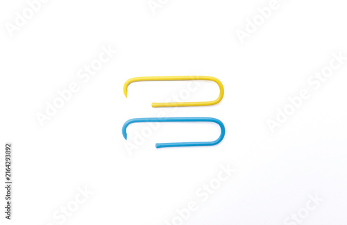 Clean composition showing two large paperclips, one blue and one yellow, attached to the edge of a white sheet.