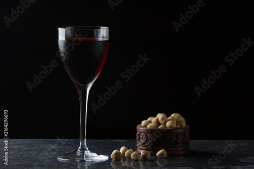 Glass of Red Wine with Roasted Hazelnuts on Dark Table in Low Key Lighting