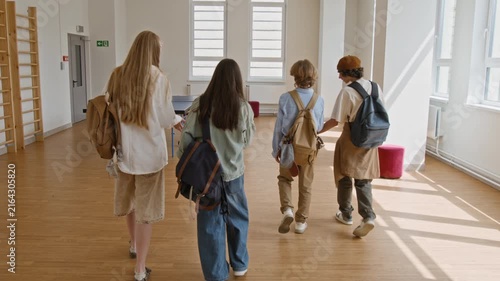 Rear view of diverse teenagers with backpacks walking through school recreation room past ping pong table. Footage is ideal for high school enrollment promos and educational marketing campaigns