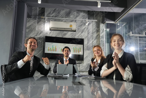 Obraz na płótnie Two thumbs up across the table from both businessmen as the ginger haired colleague claps, upbeat teamwork celebration under the analytics screen at night in a bright modern coworking