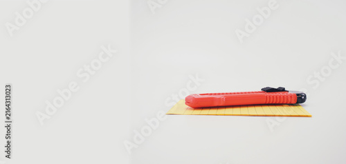 Taglierino in plastica di colore arancio e fogli di carta gialla per appunti su una superficie bianca e vuota con spazio testo