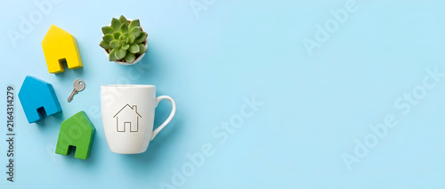Colorful wooden house models, a cup with a house icon, keys, and a succulent on a blue background representing real estate and planning