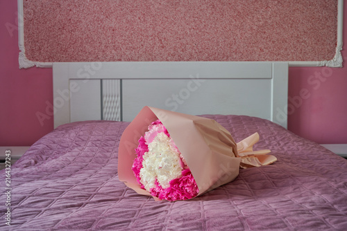 Beautiful bouquet of pink and white flowers lying on a bed in a pink bedroom, Beautifully wrapped floral bouquet on a made bed with white headboard