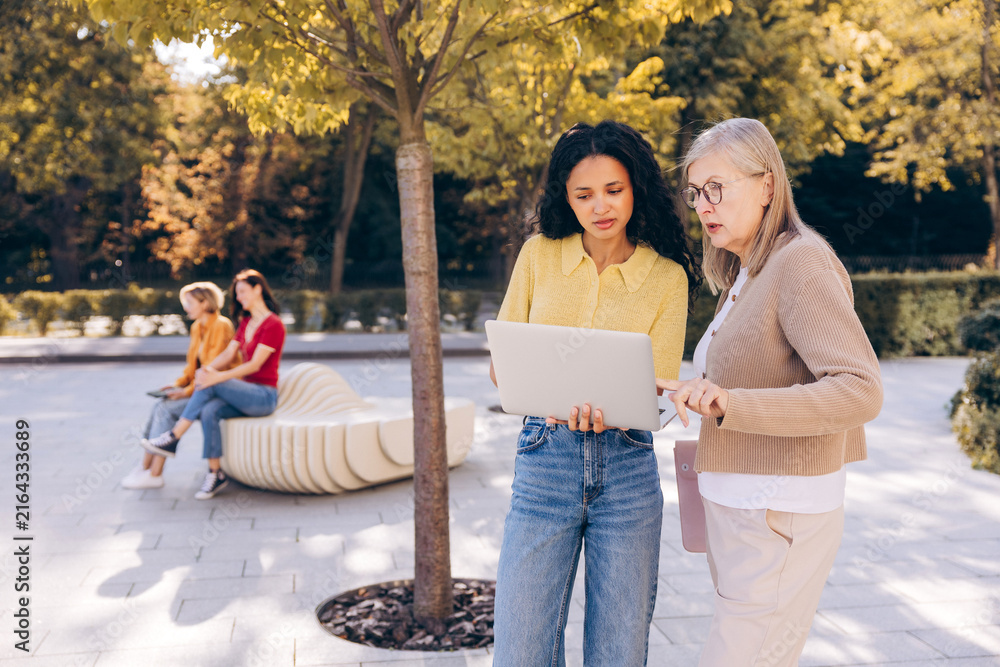 Naklejka premium Beautiful senior and young African American women using laptop working on the street outdoors