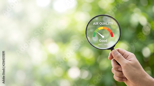 Hand holding magnifying glass over air quality meter showing good levels