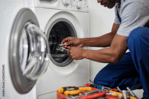 Black man in blue overalls works on broken domestic equipment