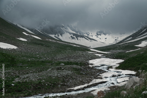 Bild auf Leinwand Moody Mountain Valley With a Winding Meltwater Stream Under a Dark Sky