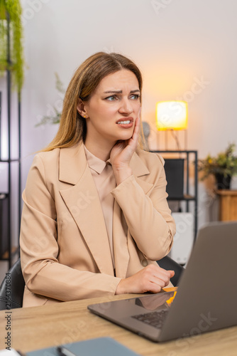 Cuadro en lienzo Middle-aged businesswoman at home office works on laptop feels tooth pain winces holds cheek tries to stay focused