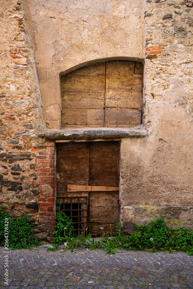 Fototapeta premium Ancient barred wooden door and stone architecture in Garessio, Piedmont, Italy.