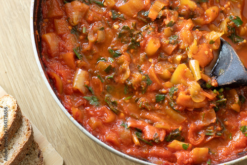 Tomato pepper sauce in a cooking pan with homemade bread on a wooden table. Top view.