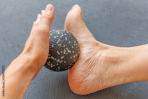 Close up of hand rolling fascia massage ball on arch of bare foot on exercise mat, plantar fasciitis and myofascial release concept
